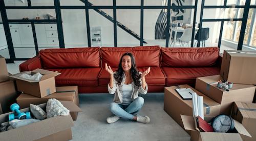 Woman sitting on floor of new house smiling with boxes around 