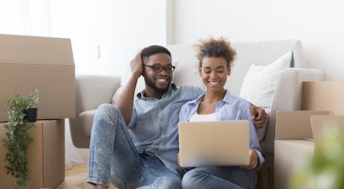 Smiling couple looking at laptop while surrounded by moving boxes