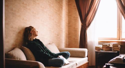 Sad girl sitting on couch looking out window