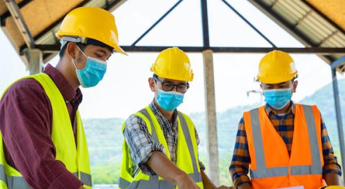 Three home builders review blueprints while wearing face masks