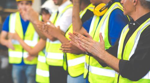 This photo shows a row of construction workers clapping.