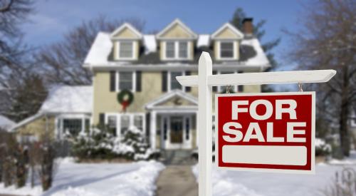 House covered in snow with for sale sign