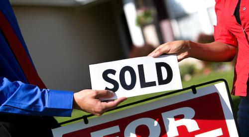 Two people placing sold sign on home for sale sign 