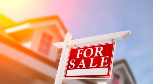 A 'For Sale' sign in front of a house with dormer windows.