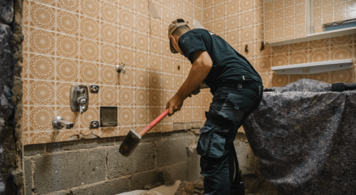 Worker swings sledge hammer to demolish bathroom for home remodel