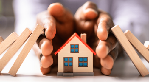 Black homeowner's hands protecting home from falling dominoes