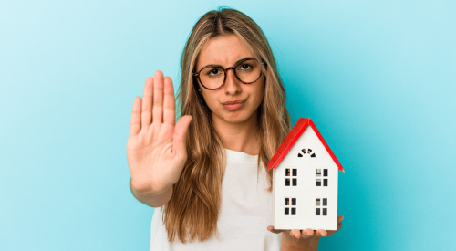 Woman holding model of a home says stop to homeownership