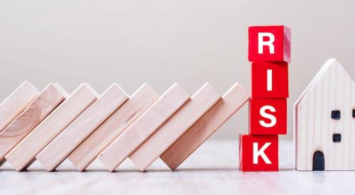 Wooden blocks are leaning toward a small house and a stack of blocks that spell out 'risk'.