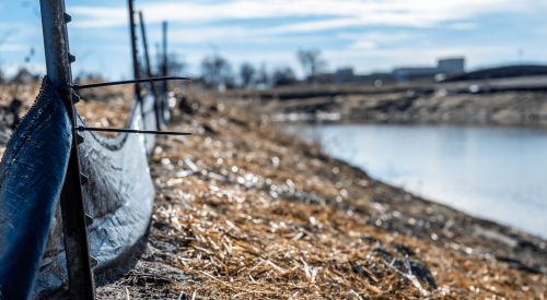 Silt fence at a construction site with straw covered dirt and retention pond in background to manage stormwater