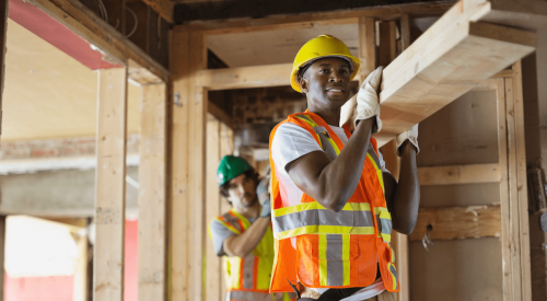 Two tradesmen carrying lumber on construction site