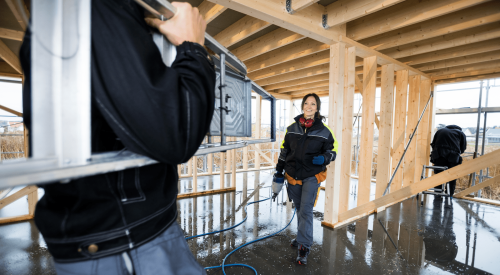 Woman skilled tradesperson on jobsite framing house with pneumatic nailer