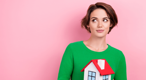 Woman renter holding model house in her hands gives a sidelong glance