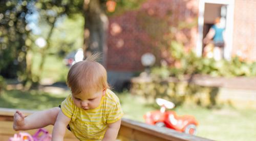 Little kid getting out of sandbox outside in backyard