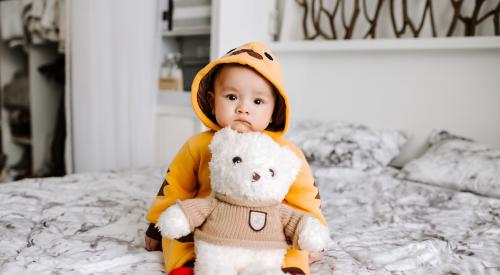 Child seated on bed with teddy bear