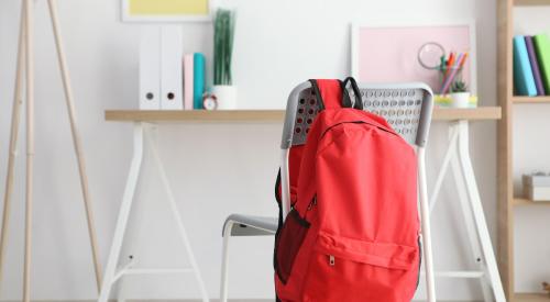 Red backpack hanging on chair in bright home workspace