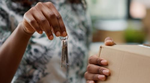 Black homeowners holding house keys and moving box