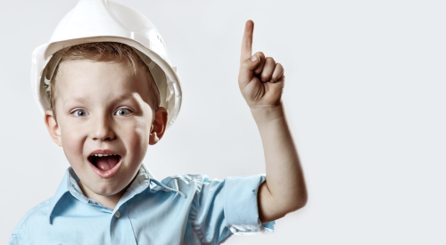 Boy wearing hard hat points upward, looking amazed