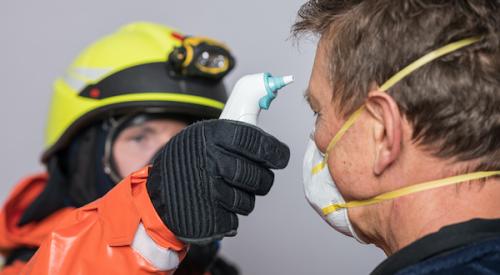 Man in protective gloves measures temperature of man wearing face mask