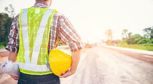 Home builder holding floor plan and hard hat while looking at lot