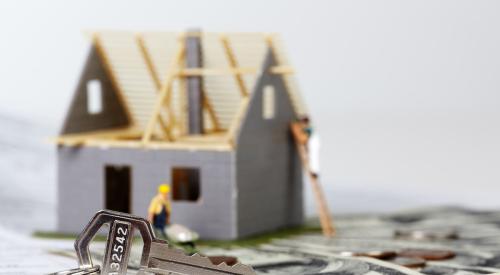 Small toy house under construction with builder figurines and a stack of cash