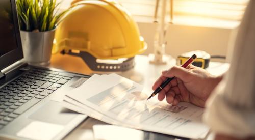 Home builder with hard hat on desk reviewing projections and data