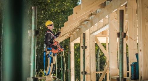 Builder on scaffolding working on home roof framing