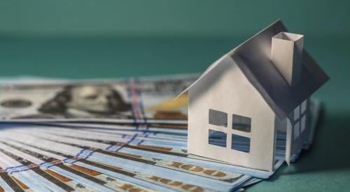 Small white house on stack of cash with green background