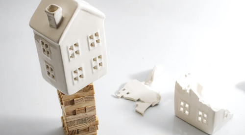 Ceramic model house teetering on Jenga blocks, danger of falling and breaking