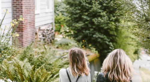 Two women walking down street near a home