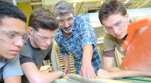 Students using saw in wood shop class in school