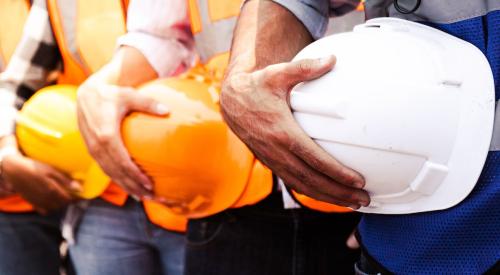 Row of tradespeople holding construction hard hats