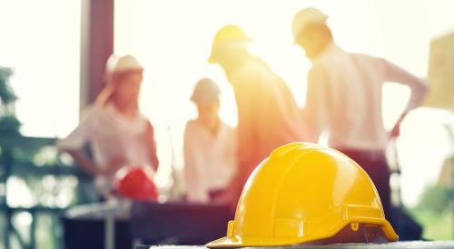 Yellow construction hard hat on table in crowded workshop