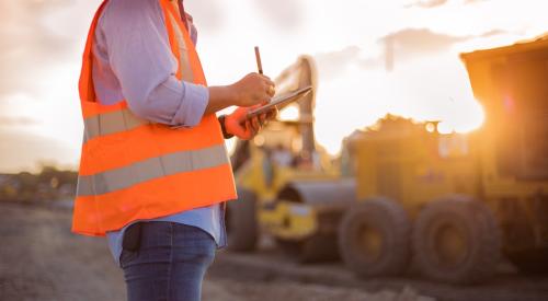 Construction worker in orange vest making notes on a tablet