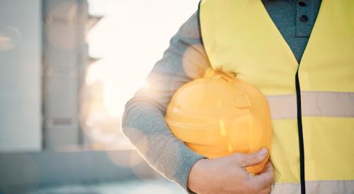 Construction worker in yellow vest holding hard hat at hip