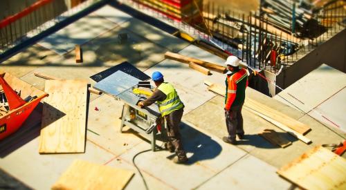 Construction workers cutting plywood panels on jobsite 