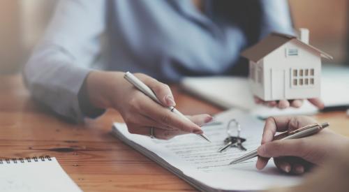 Person signing housing contract with house model and keys on table