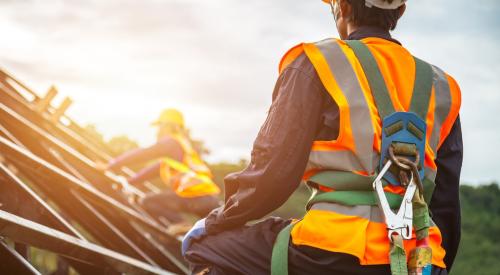 Person working on roof of new home with fluorescent vest and safety harness 