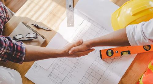 Contractor and client shaking hands above desk with paperwork on it