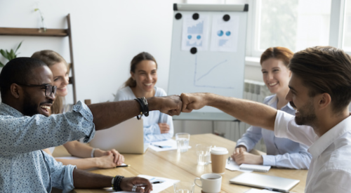 Coworkers fist bumping at a conference table show teamwork and positive company culture