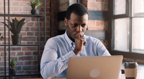 A businessman sitting at a desk using a laptop crafts crisis messaging for his business 