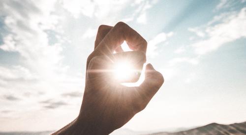 Person's hand in front of landscape and sun