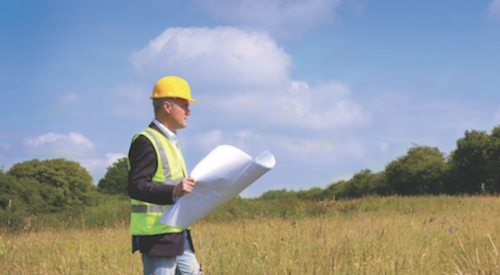 Developer stands in green field holding plans for future development 