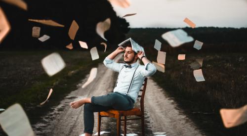 man sitting on chair on road with papers flying everywhere