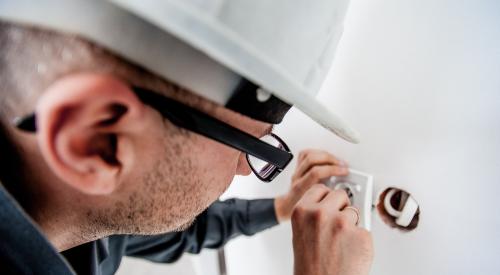 construction worker wearing hard hat installing electrical outlet in wall