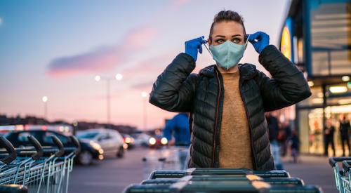 woman wearing protective face mask and latex gloves with shopping carts in carpark outside grocery store 