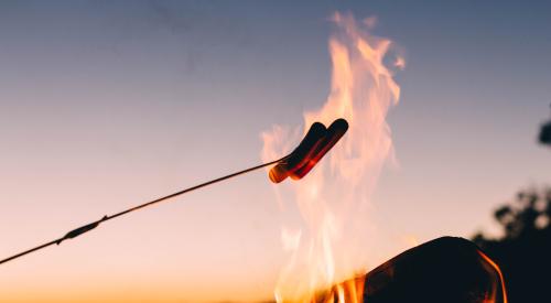 Roasting hot dogs on open flame at twilight