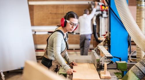 Female carpenter running wood through saw