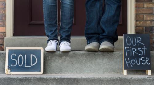 Couple standing on front porch with signs that read "sold" and "our first house"