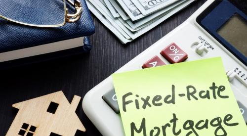 Yellow post-it with "fixed-rate mortgage" written on it next to calculator, small wooden house, and stack of cash