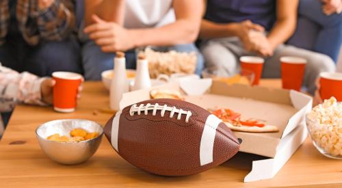 Living room coffee table covered in snacks and drinks with a football in the foreground